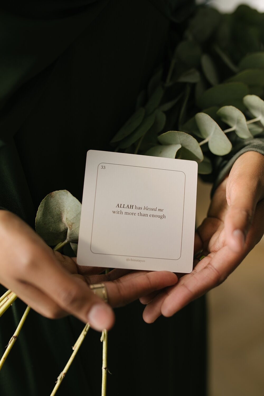 A woman holding a card with eucalyptus leaves and Chinutay & Co daily affirmation cards